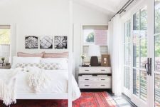 a white mid-century modern bedroom with a canopy bed, whitewashed nightstands, a black and white gallery wall, a red printed rug and a glazed wall