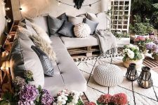 a wonderful outdoor space with a pallet corner bed, lots of blooms, string lights, a dream catcher, neutral pillows and upholstery and greenery