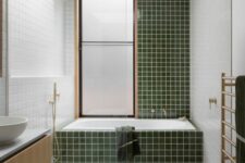an airy mid-century modern bathroom with a terrazzo floor, green and white tiles, a bathtub, a floating vanity and gold fixtures