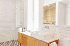 an airy mid-century modern bathroom with mosaic tiles on the floor and white subway ones on the walls, a wooden vanity and mid-century lamps