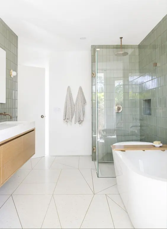 an airy mid-century modern bathroom with white geo and green skinny tiles, a floating vanity and a tub, a shower space