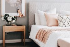 an airy mid-century modern bedroom with grey walls and a tan floor, a grey upholstered bed, neutral bedding, a little nightstand, a copper lamp and a chic print