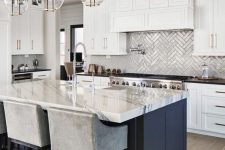 an elegant kitchen with white shaker cabinets, a navy kitchen island with a dining space, chrome fixtures and appliances and gold and glass pendant lamps