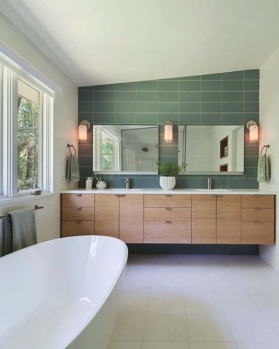 An elegant mid century modern bathroom with green and white tiles, a large double vanity built in, two mirrors and a large tub