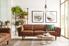 an elegant mid-century modern living room with brown leather sofas, an open shelving unit, a low coffee table and lots of greenery