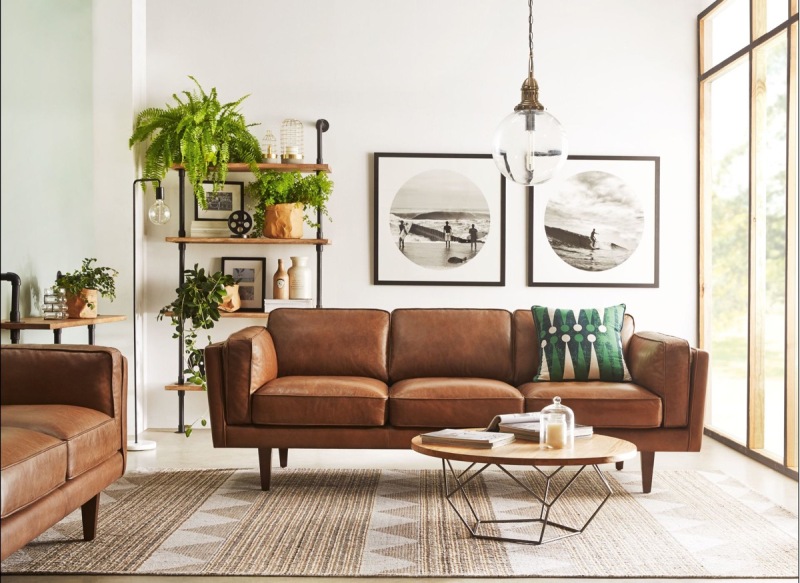 an elegant mid century modern living room with brown leather sofas, an open shelving unit, a low coffee table and lots of greenery