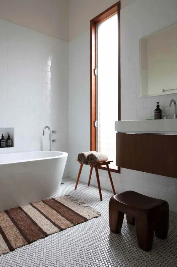 An ethereal mid century modern bathroom with white penny and subway tiles, an oval tub, a floating vanity and a wooden stool