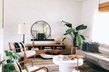 an inviting mid-century modern living room with a grey sofa, creamy chairs, a stained storage unit, round tables and statement plants