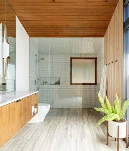 Neutral wooden floors, white skinny tiles and wooden paneling on the walls and ceiling, a floating wooden vanity and a potted plant to compose a mid century modern bathroom