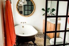 03 a beautiful eclectic bathroom with white walls, black and white Moroccan tiles, a black clawfoot tub, a neutral vanity, a black glass shower wall, a bold pompom bench