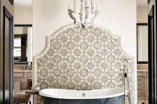 13 a refined bathroom with geo and Moroccan tiles, a metal clad bathtub, a mirrored chandelier and some neutral furniture