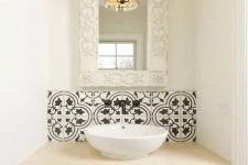 18 a small bathing space with a vanity clad with black and white Moroccan tiles and a backspalsh, a chic mercury glass pendant lamp and a whitewashed frame