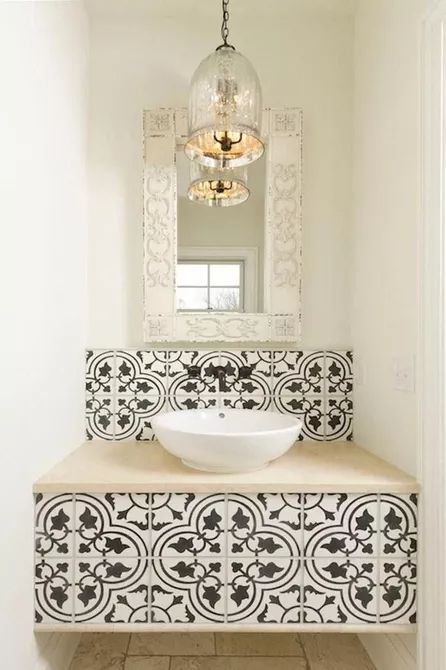 a small bathing space with a vanity clad with black and white Moroccan tiles and a backspalsh, a chic mercury glass pendant lamp and a whitewashed frame