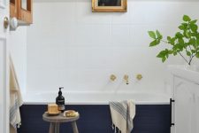21 a stylish modern bathroom with blue Moroccan tiles, a bathtub clad with navy tiles, a cabinet, an artwork and a white vanity