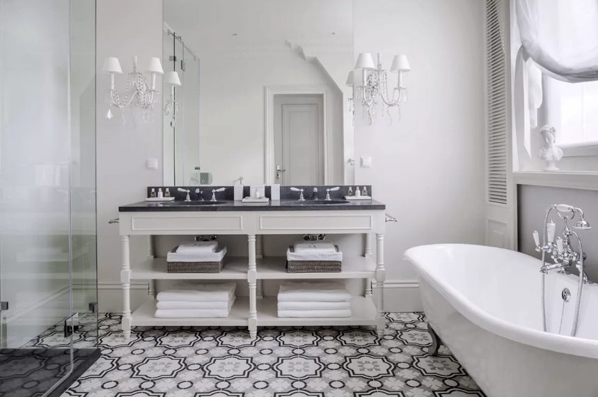 a vintage black and white bathroom with a neutral vanity, black countertops, a shower space, a vintage tub, vintage sconces and shutters on the wall