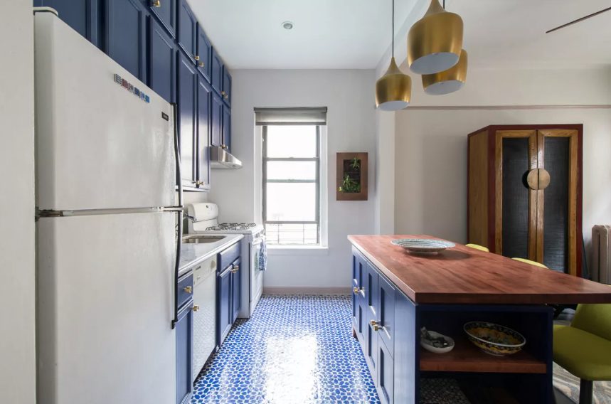 a bold navy kitchen with butcherblock countertops, bold blue Moroccan tiles on the floor, brass pendant lamps and white appliances