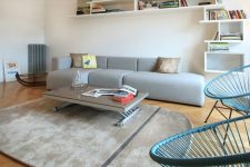 a Scandinavian space wiht a grey low sofa, a grey rug, blue chairs, a low coffee table and a large shelving unit is wow