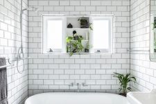 a beautiful black and white bathroom with white subway and black hex tiles, a free-standing sink, a black vintage bathtub and a window