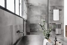 a beautiful contemporary bathroom clad with concrete tiles, with a shower space, a metal bathtub and a black stone stool is gorgeous