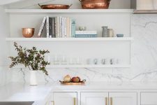 a beautiful white kitchen with shaker cabinets, white countertops and a white stone backsplash, white floating shelves and copper touches