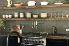 a black kitchen with concrete countertops and a concrete kitchen wall, floating shelves and black fixtures
