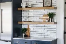 a blue farmhouse kitchen with a white subway tile backsplash and countertops, thick floating shelves and a large stained kitchen island