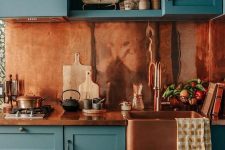 a blue shaker style kitchen with a rich-stained countertop and a copper backsplash is a very bold and catchy idea
