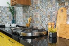 a bold kitchen with yellow and stained cabinets, black countertops, a colorful Moroccan tile backsplash and neutral fixtures