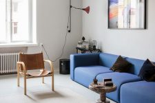 a bold mid-century modern living room with a bright blue low sofa, leather chairs, a stone coffee table and a bright artwork