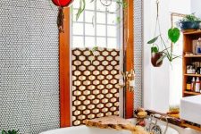 a bright bathroom with penny tiles, rich-stained wooden beams, a clawfoot tub, a floating vanity and a wooden bookshelf plus lots of potted plants