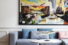 a bright living room with a grey low sofa, a colorful artwork, pastel pillows, a round table is a very cool and bold space