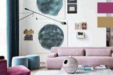 a bright living room with a pale pink low sofa, a purple chair and blue poufs, a watercolor gallery wall and a low coffee table looks cool