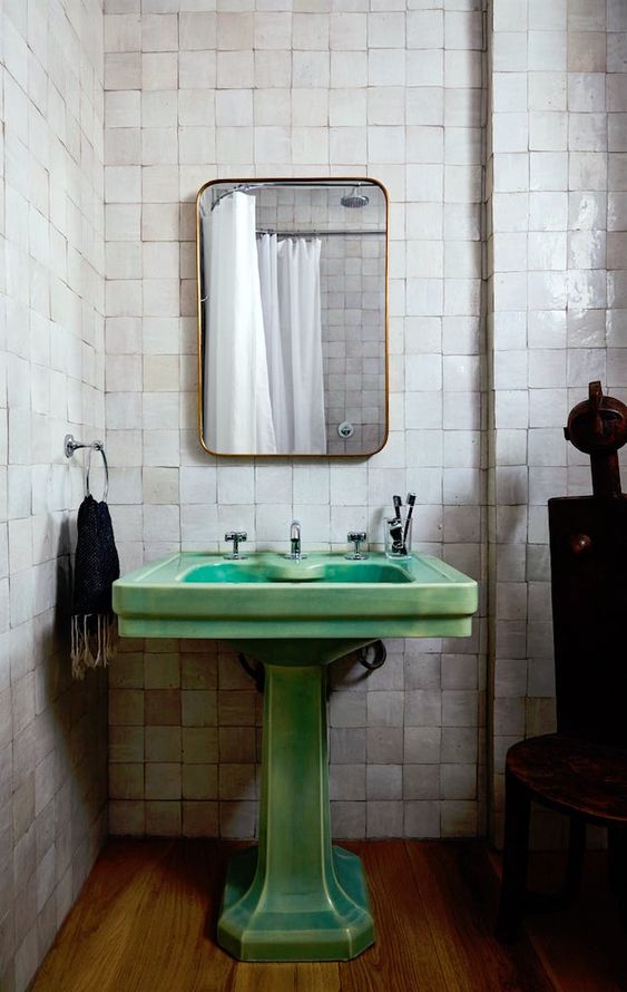 a catchy bathroom with grey glazed tiles, a green pedestal sink, a mirror in a gilded frame and dark touches for a chic look