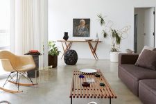 a catchy living room with a brown low sofa, a leather chair, a bench as a coffee table and a console table plus potted plants