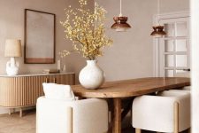 a chic Japandi dining room in neutrals with a lovely wooden slab credenza, a rounded table and neutral chairs, pendant lamps and a cool artwork