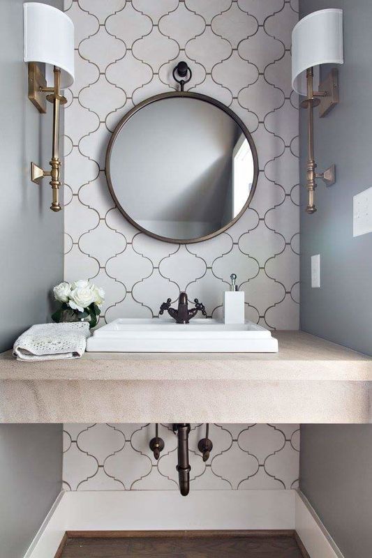 a chic and refined bathroom in neutrals, with grey walls and a white arabesque tile accent wall, a round mirror, chic sconces is amazing