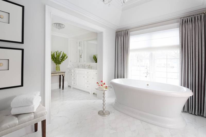 a chic and refined bathroom with a floor clad with marble arabesque tiles, a vintage bathtub, a white vanity and a leather bench plus a large window