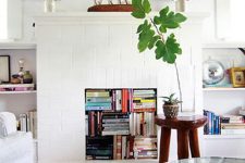 a chic living room with a white tile fireplace, books stored inside it and on the built-in shelves around, potted plants and lamps
