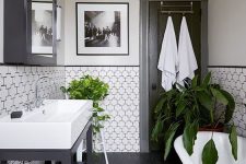 a chic vintage black and white bathroom with catchily shaped tiles and black penny ones, a console sink, a clawfoot tub and a black mirror cabinet