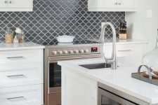 a chic white kitchen with shaker style cabinets, a graphite grey arabesque tile backsplash for a contrast and elegantly built-in appliances
