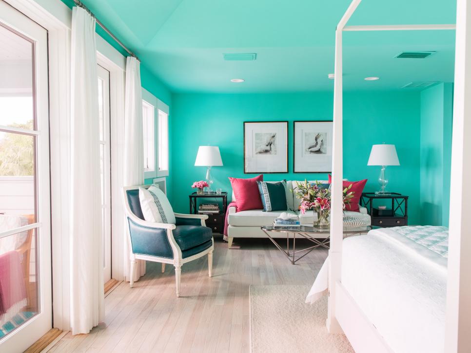 a colorful bedroom with turquoise walls and a ceiling, a white canopy bed, a creamy sofa with colorful pillows, a navy chair and a gallery wall