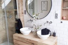a contemporary bahtroom clad with white subway tiles, wood look tiles in the shower, a wooden vanity, round sinks and a round mirror