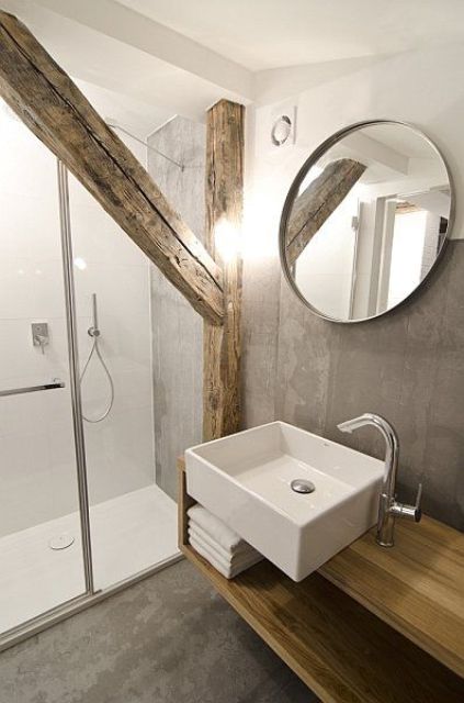 a contemporary bathroom clad with concrete, with a wooden pillar and beam, a floating vanity, a round mirror and a sink