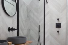 a contemporary bathroom clad with grey wood look tiles, with grey round sinks, a round mirror, a glass wall and black fixtures