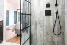 a contemporary bathroom clad with hex white stone tiles and wood look ones, with black fixtures and a glass framed wall is cool