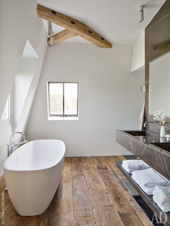 a contemporary bathroom in white, with a weathered wood floor, a wooden beam, a black marble floating vanity and a large mirror