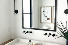 a contemporary bathroom with a floating vanity, a white stone vessel sink, a mirror in a black frame and black fixtures is cool