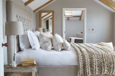 a contemporary bedroom with light-stained wooden beams, a grey upholstered bed, neutral bedding, a wooden chest nightstand