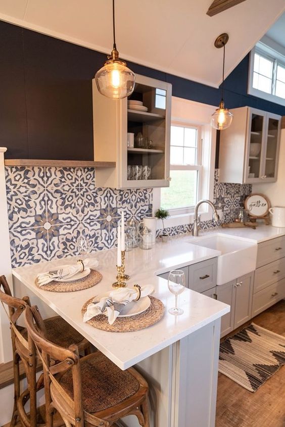 a contemporary grey kitchen with white countertops, blue Moroccan tiles on the backsplash and glass cabinets