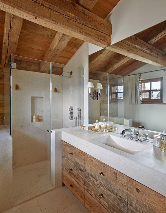 a contemporary neutral bathroom with a wooden roof and beams, with a wooden vanity, neutral stone and matching tiles plus a large mirror